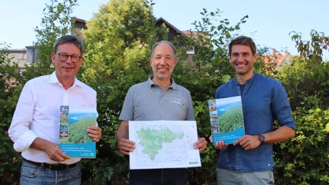 Drei Personen halten zwei Bücher und eine Karte hoch