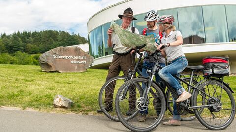 Ranger zeigt zwei Radfahrern etwas auf einer Karte