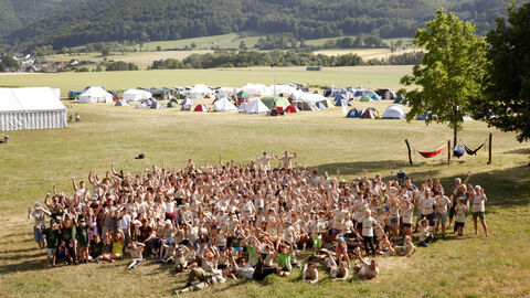 Gruppenbild mit vielen Personen und Zeltlager im Hintergrund