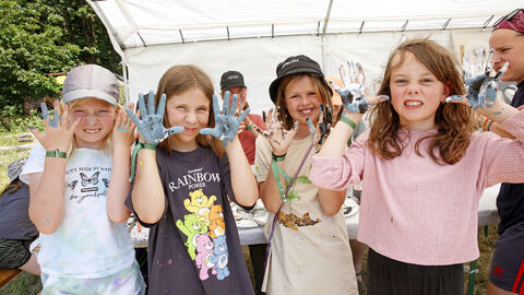 Mehrere Kinder stehen zusammen und halten ihre mit Farbe bemalten Hände in die Kamera