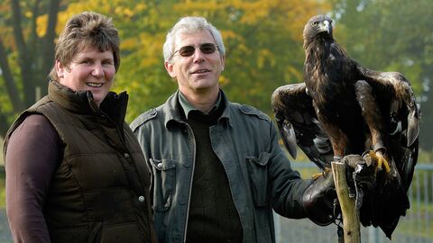 Zwei Personen stehen nebeinander. Eine der Personen hält einen Greifvogel auf der Hand.