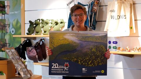 Ab sofort erhältlich: Anna Wiedemann präsentiert den Wandkalender 2024 mit dem Titel „20 Jahre Nationalpark Kellerwald-Edersee“. Er ist in den Shops des WildtierParks Edersee und des NationalparkZentrums Kellerwald sowie in Buchhandlungen der Region zu erwerben. Eine Person hält den Nationalpark-Wandkalender in die Kamera