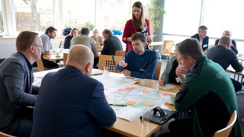 Nationalparkplanung Menschen sitzen in Gruppen an Tisch und tauschen sich über verschiedene Ideen aus