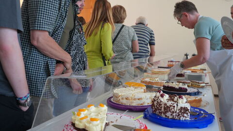 Kuchenbuffet der Altenlotheimer Hausfrauen: Die leckeren Torten und Kuchen fanden wieder reißenden Absatz Auf einer langen Tafel stehen hinter einer Scheibe viele Torten. Gäste gehen daran vorbei und suchen sich Kuchen aus