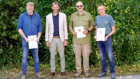 Kennen sich seit 40 Jahren: Ralf Schramme (1.v.l.), Volker Leifels (2.v.r.) und Jochen Lückel (1.v.r) feierten am Freitag, 1. August, gemeinsam ihr 40-jähriges Dienstjubiläum. Nationalparkleiter Manuel Schweiger (2.v.l.) überreichte den Jubilaren aus diesem Anlass ihre Urkunden während einer kleinen Feierstunde. Die drei Jubilare stehen mit ihren Urkunden in den Händen gemeinsam mit Nationalparkleiter Schweiger vor einer grünen Hecke
