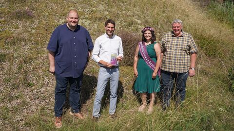 Heideblütenprinzessin Saija I (mit Schärpe) eröffnet die neue Heide-Route mit Bürgermeister Frankenau (links), Nationalparkleiter und Ortsvorsteher Altenlotheim (rechts) Die Heideblütenprinzessin mit Schärpe steht mit drei Männern vor einem bewachsenen Hügel und alle lächeln in die Kamera, das Heidekraut blüht auch.