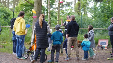 Im WildtierPark steht Gerd der Gaukler mit einer Gruppe Menschen, von denen ein paar bunte Teller auf einem senkrechten Stock über ihren Köpfen balancieren.
