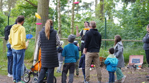 Im WildtierPark steht Gerd der Gaukler mit einer Gruppe Menschen, von denen ein paar bunte Teller auf einem senkrechten Stock über ihren Köpfen balancieren.
