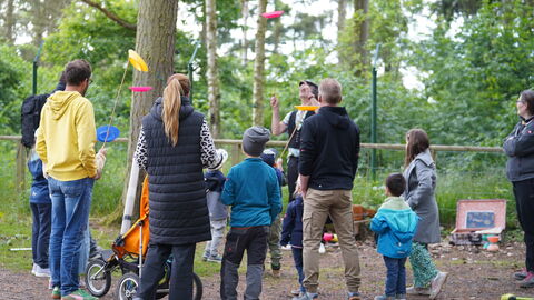 Im WildtierPark steht Gerd der Gaukler mit einer Gruppe Menschen, von denen ein paar bunte Teller auf einem senkrechten Stock über ihren Köpfen balancieren.