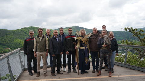 Gruppenfoto mit 11 Personen auf der Aussichtsplattform: sie lächeln in die Kamera, einige tragen Outddorkleidund, die Falknerinhält eine Eule auf der Hand und eine Dame tärgt ein Fantasy-LARP-Gewand.