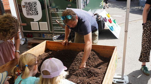 Erwachsene und Kinde beugen sich über eine mit Mulch gefüllte Sandkiste udn suchen Sachen