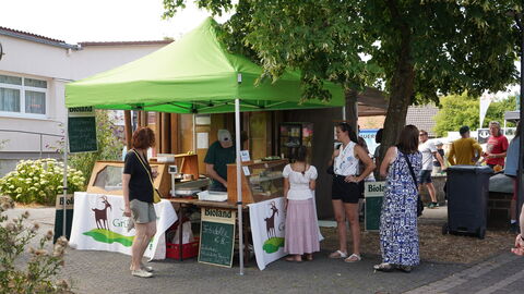 Ein hellgrüner Pavillon mit Verkaufsstand darunter, es stehen Leute an, die etwas kaufen wollen