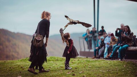 Falknerin und Kind stehen mit Greifvogel auf einer Flugwiese